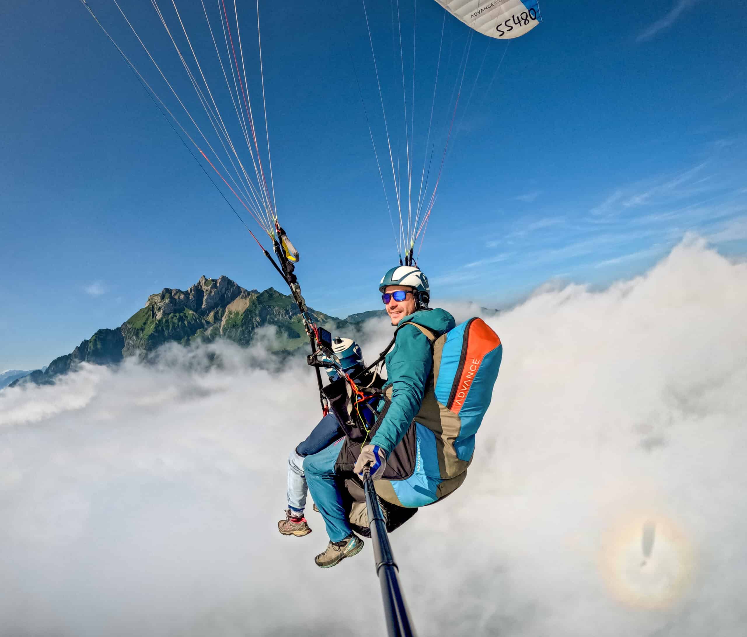 Pilot und Passagier beim Tandemflug betrachten den wolkenverhangenen Pilatus, mit Halo am Himmel und glücklichem Piloten – beeindruckende Stimmung