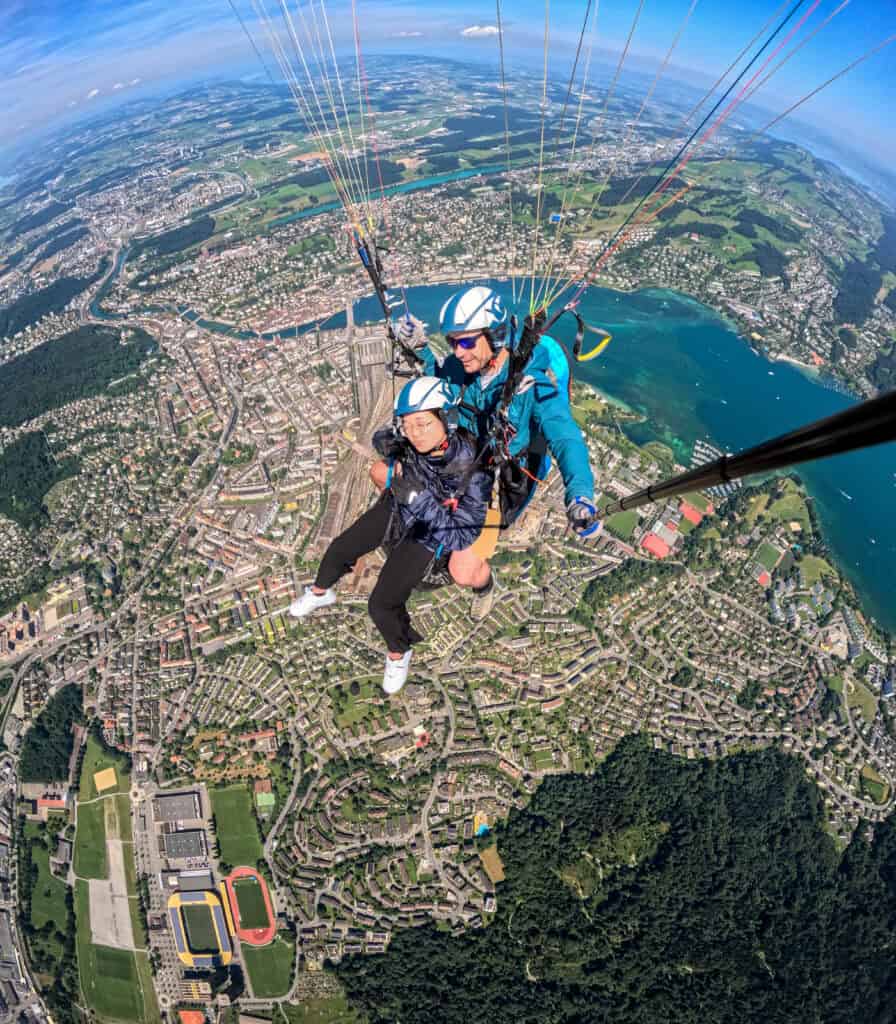 Junger Passagier beim Tandemflug eineinhalb Kilometer über Luzern, mit klarem Blick auf das helle Blau des Rotsees, die Unterwasserstrukturen im Vierwaldstättersee, Bahnhof, Seebrücke, Kapellbrücke, Museggmauer und weitere Sehenswürdigkeiten der Stadt Luzern